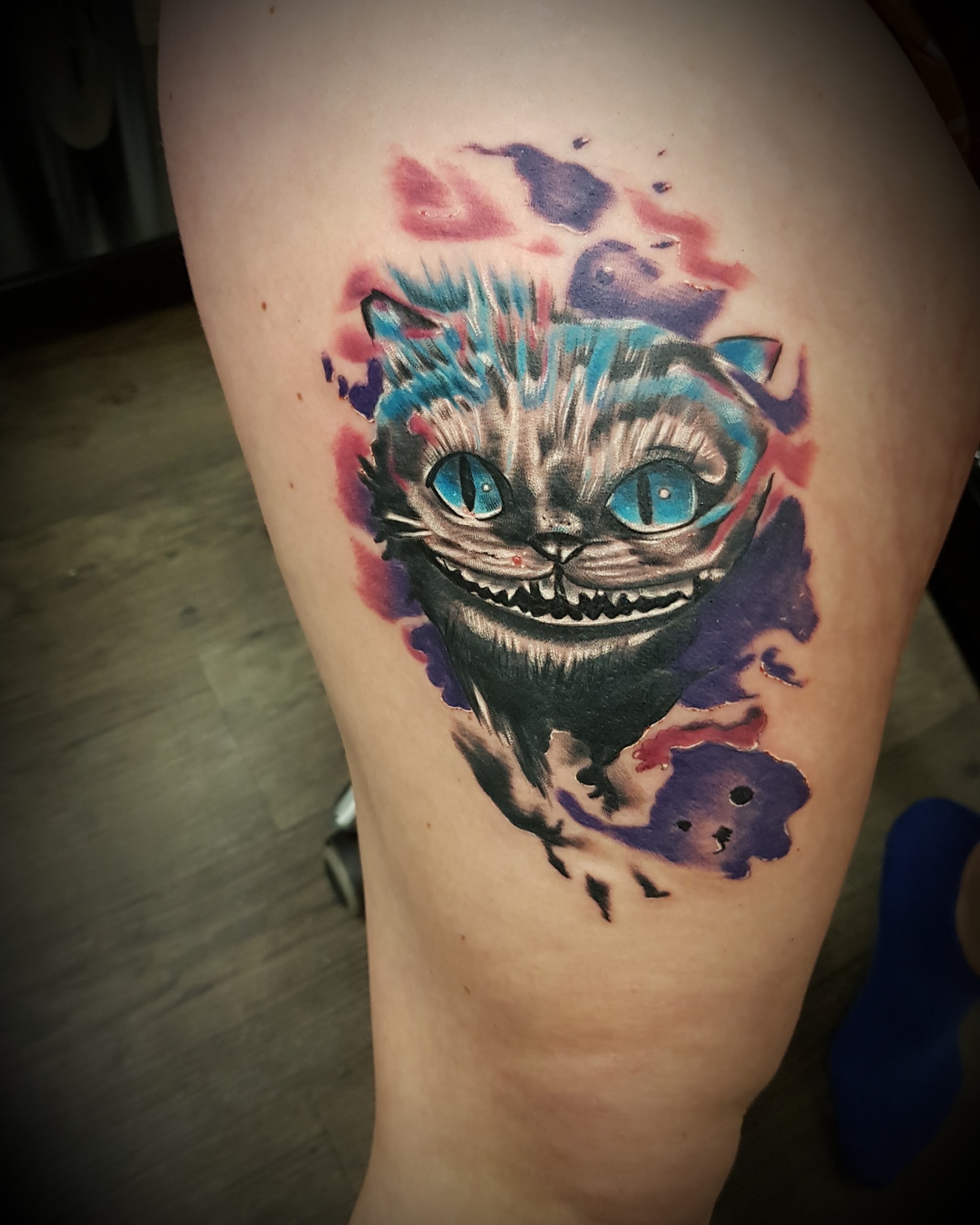 Farbtattoo auf dem Oberschenkel: grinsende Katze in Blau und Lila